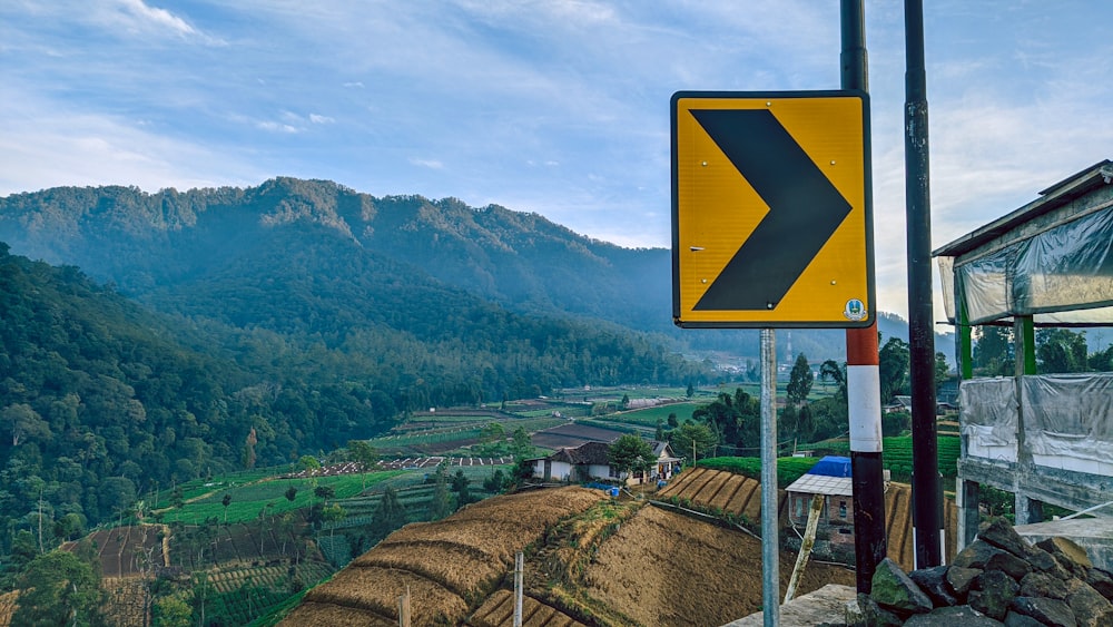 a yellow arrow sign on a pole next to a mountain