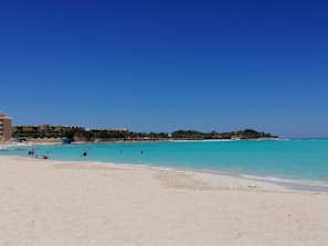 Family enjoying a sunny day at a sandy beach with clear turquoise water