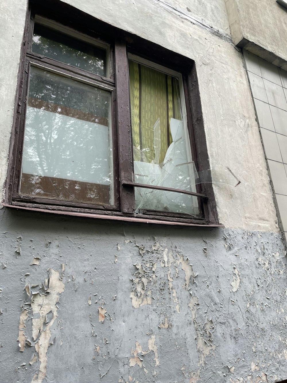 ein zerbrochenes Fenster an einem Gebäude mit einem zerbrochenen Vorhang