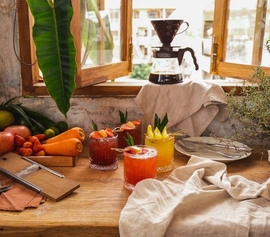 A vibrant display of fresh fruits and a glass of juice on a rustic wooden table with deep crimson and forest green accents.