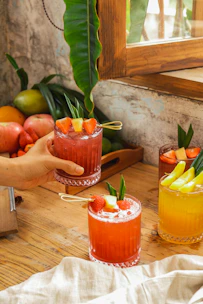 An inviting shot of a wooden table with several colorful Thai fruit drinks in clear cups.