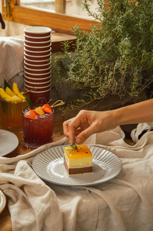 A professional caterer in black attire arranging a dessert table adorned with thyme sprigs.