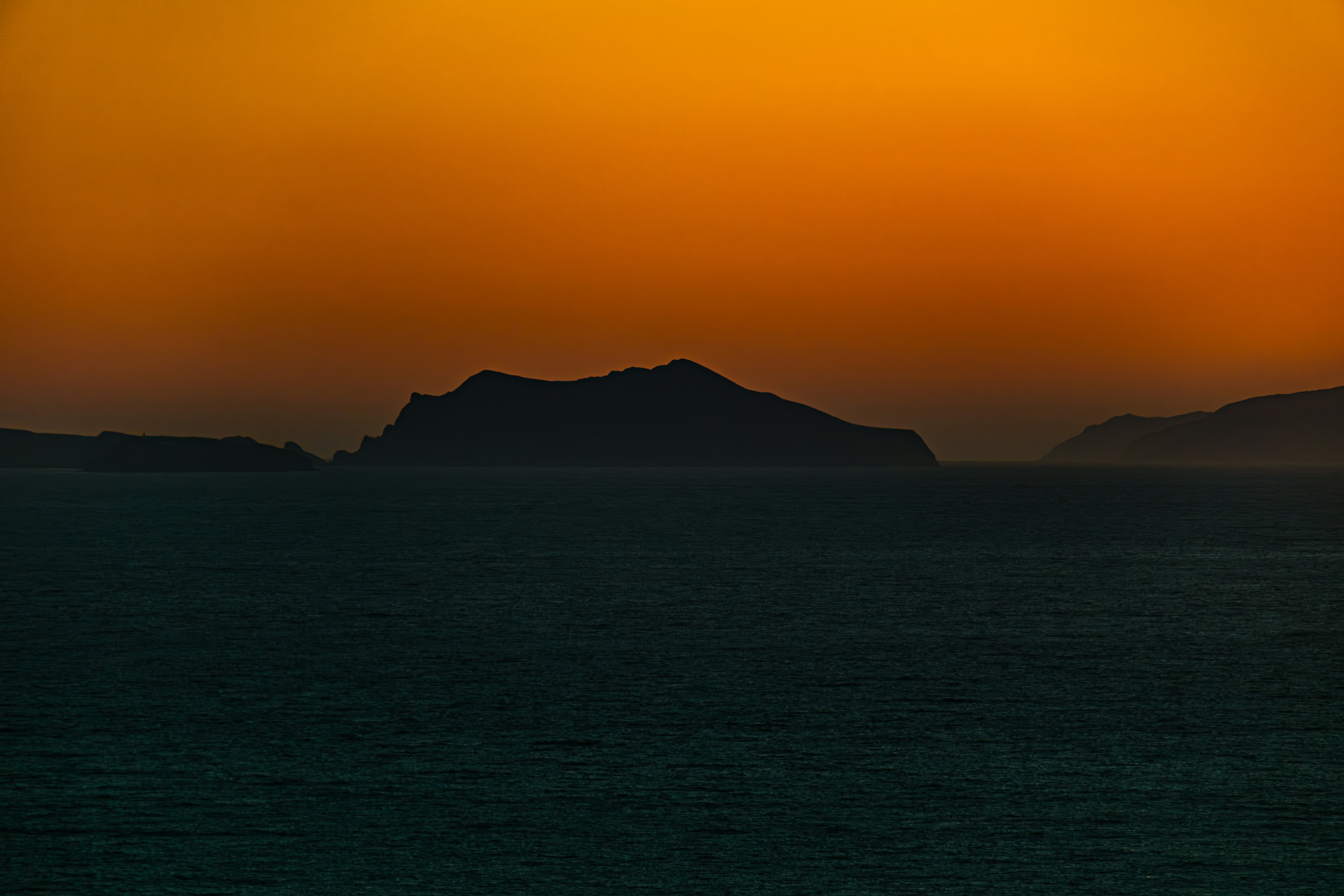 a sunset over a body of water with mountains in the distance, So close yet so far...