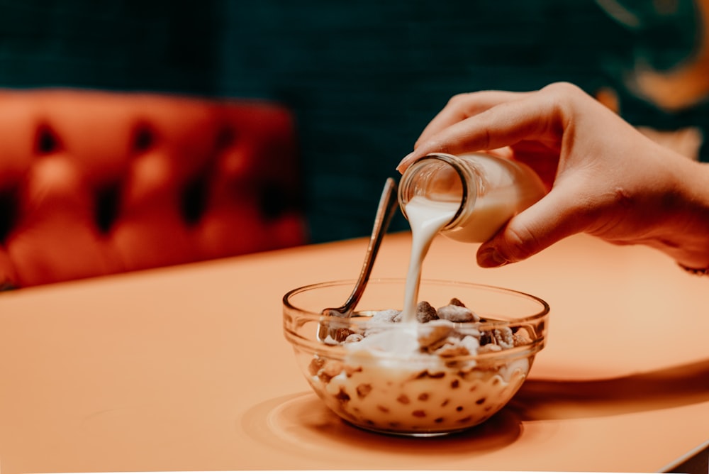a person pouring milk into a bowl of food