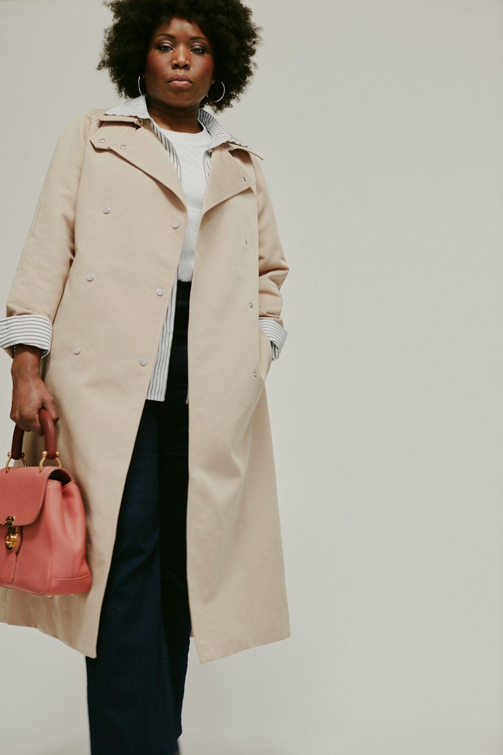 a woman in a trench coat holding a pink purse