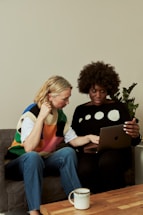 two women sitting on a couch looking at a laptop