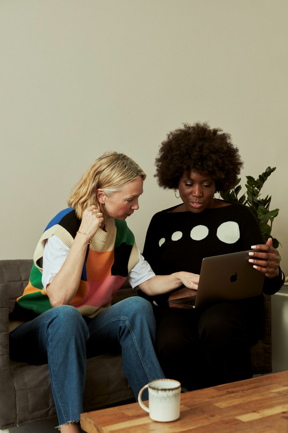 two women sitting on a couch looking at a laptop