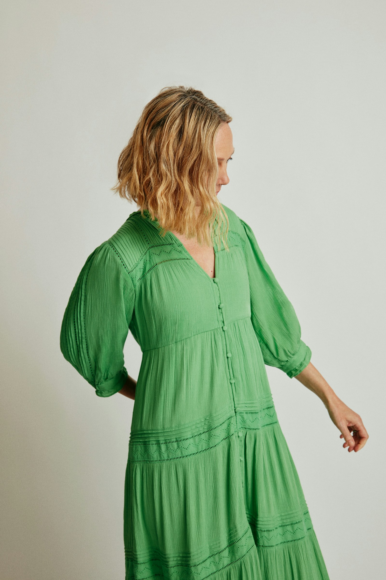 Mulher de vestido verde de mangas bufantes em fundo neutro
