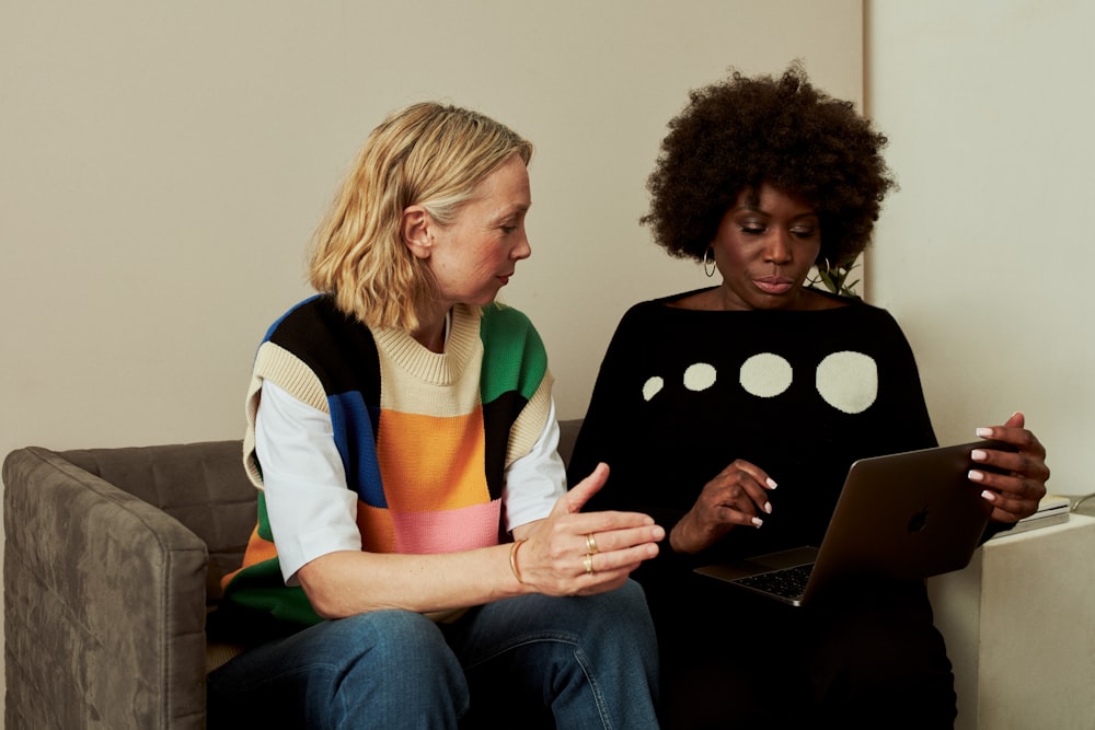 two women sitting on a couch looking at a laptop