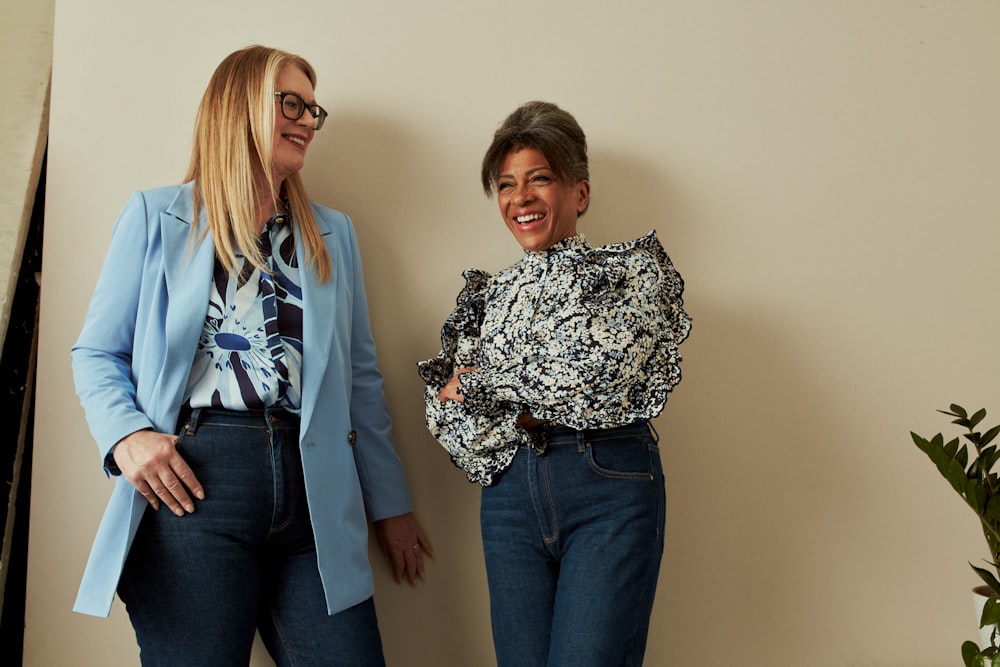 two women standing next to each other in front of a wall