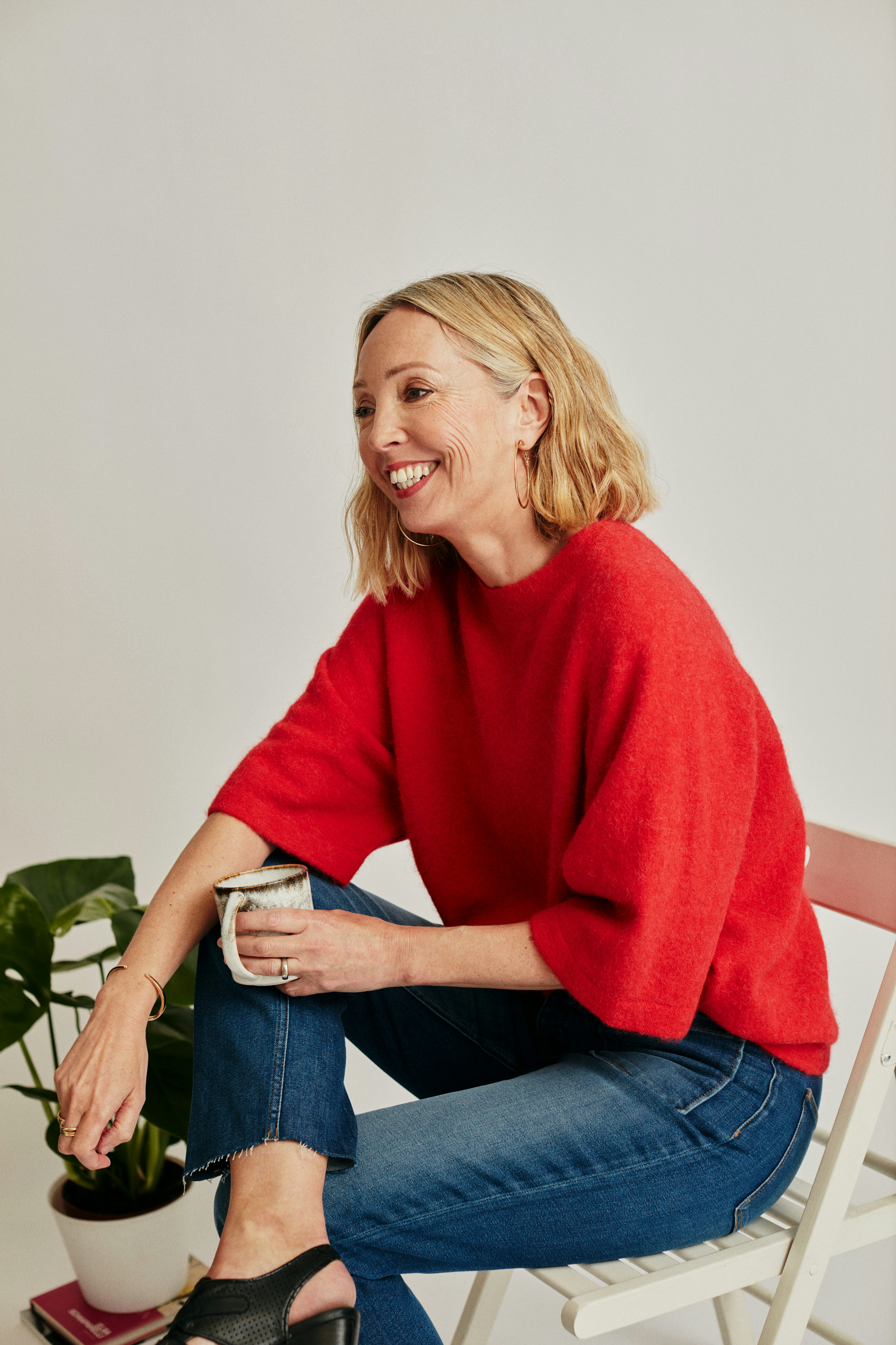 a woman in a red sweater and jeans sitting on a chair