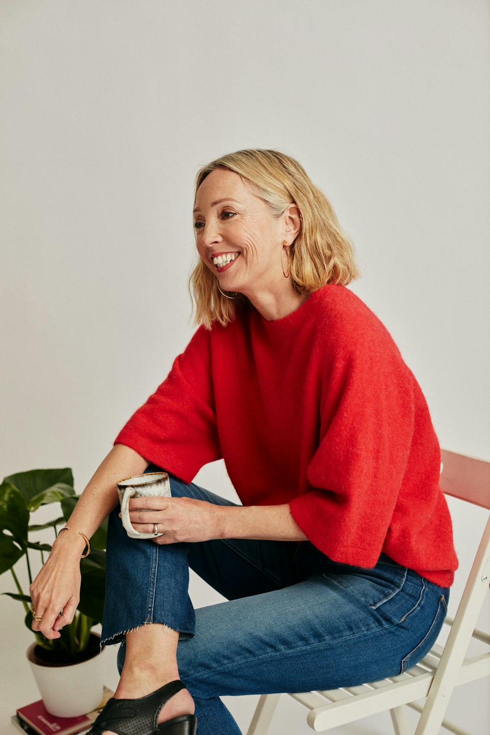 a woman in a red sweater and jeans sitting on a chair