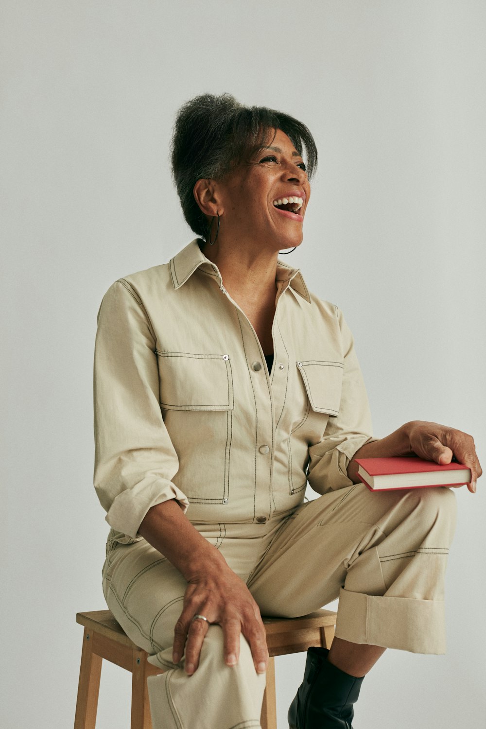 a woman sitting on a stool laughing and holding a book