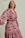 A person wearing a long-sleeve dress with a pink and black floral pattern. The dress has a wrap style, and the person appears confident with a slight smile. The background is plain and neutral, enhancing the focus on the clothing.