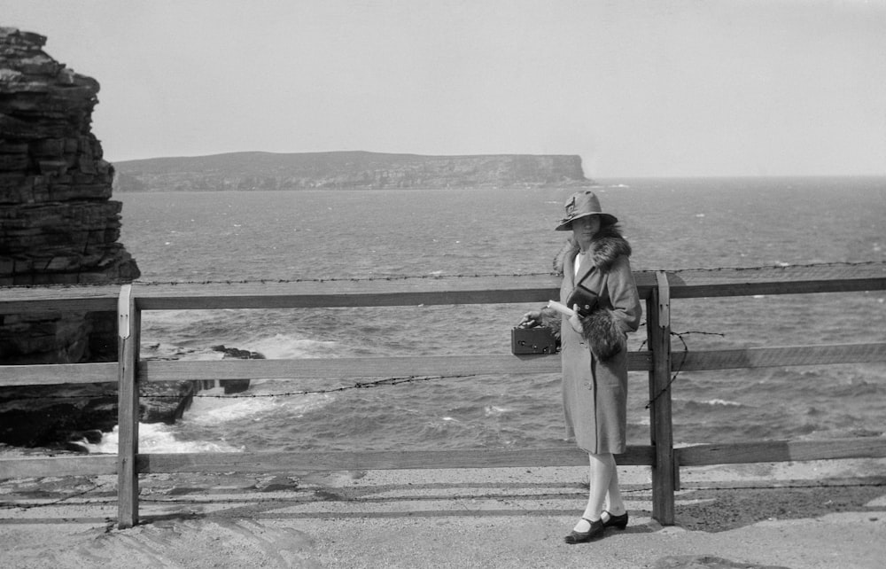 a woman standing on a fence looking out at the ocean
