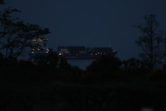 Modern cargo ship navigating calm seas under a starry night sky with laser-like light effects