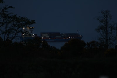 Modern cargo ship navigating calm seas under a starry night sky with laser-like light effects