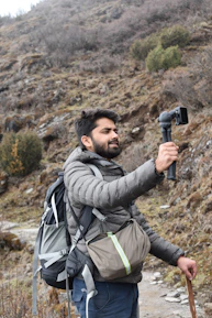 A male influencer hiking through a lush mountain trail with a camera in hand.