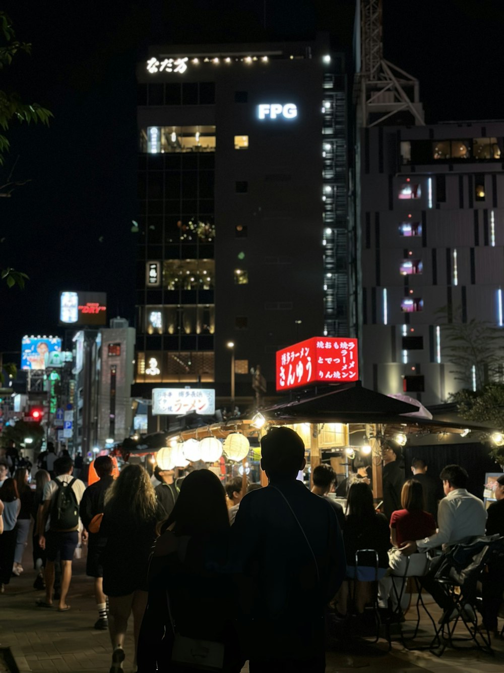 uma multidão de pessoas caminhando por uma rua à noite
