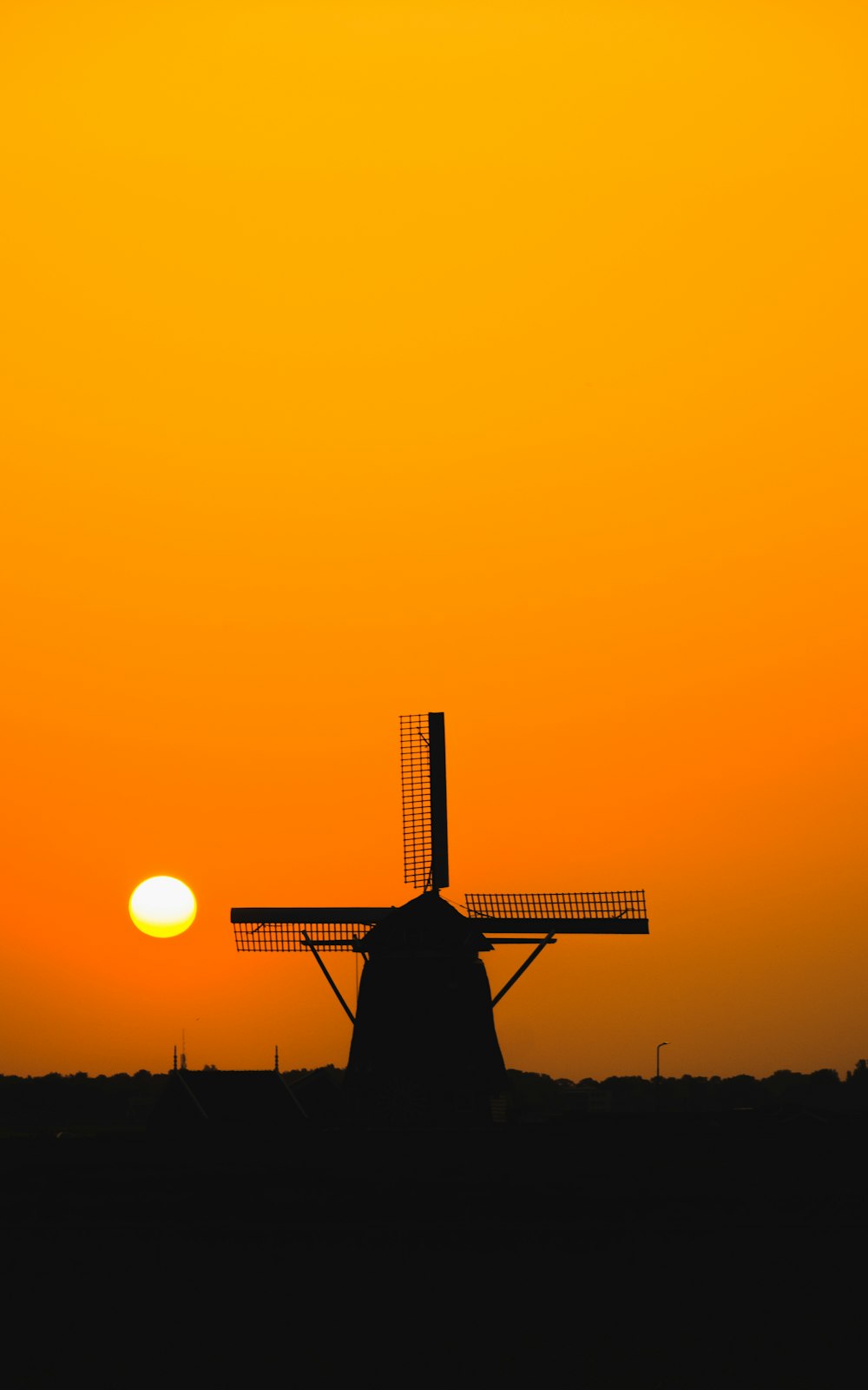 the sun is setting behind a windmill in a field