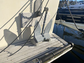 Polished silver yacht anchor resting on pristine teak wood with ocean reflections.