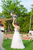 Bride in a minimalist white lace gown standing in a garden filled with blooming flowers.