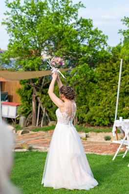 Bride in a minimalist white lace gown standing in a garden filled with blooming flowers.