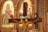 Wooden crucifix with a figure of Jesus in the foreground, set against a richly decorated golden religious icon panel featuring two saints. The carvings are intricate, and soft lighting highlights the ornate woodwork and the colorful robes on the icons.