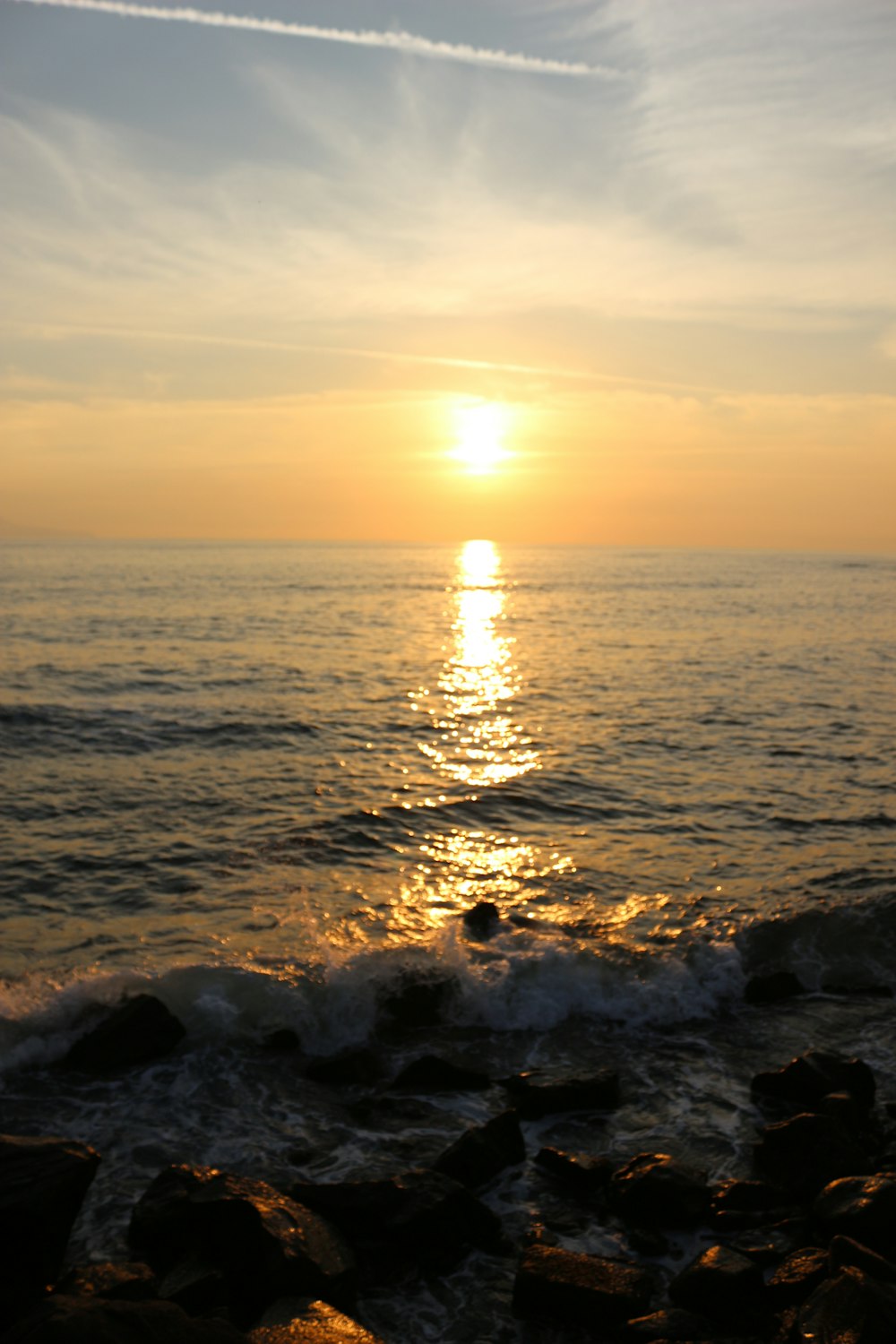 the sun is setting over the ocean with rocks in the foreground