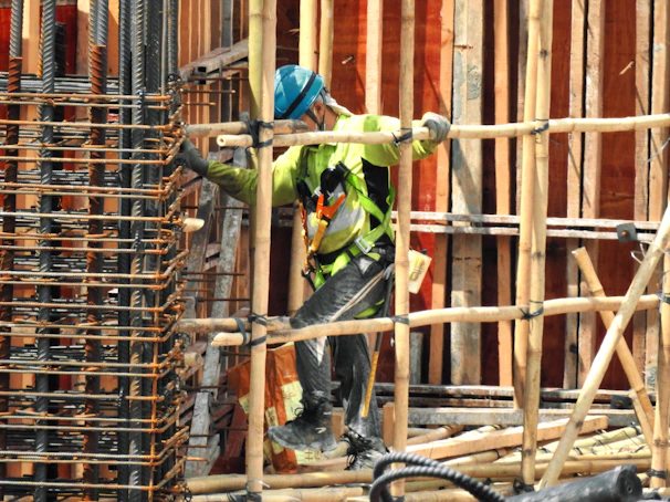 A skilled construction worker wearing a hard hat and safety vest, measuring wooden beams on a sunny site.