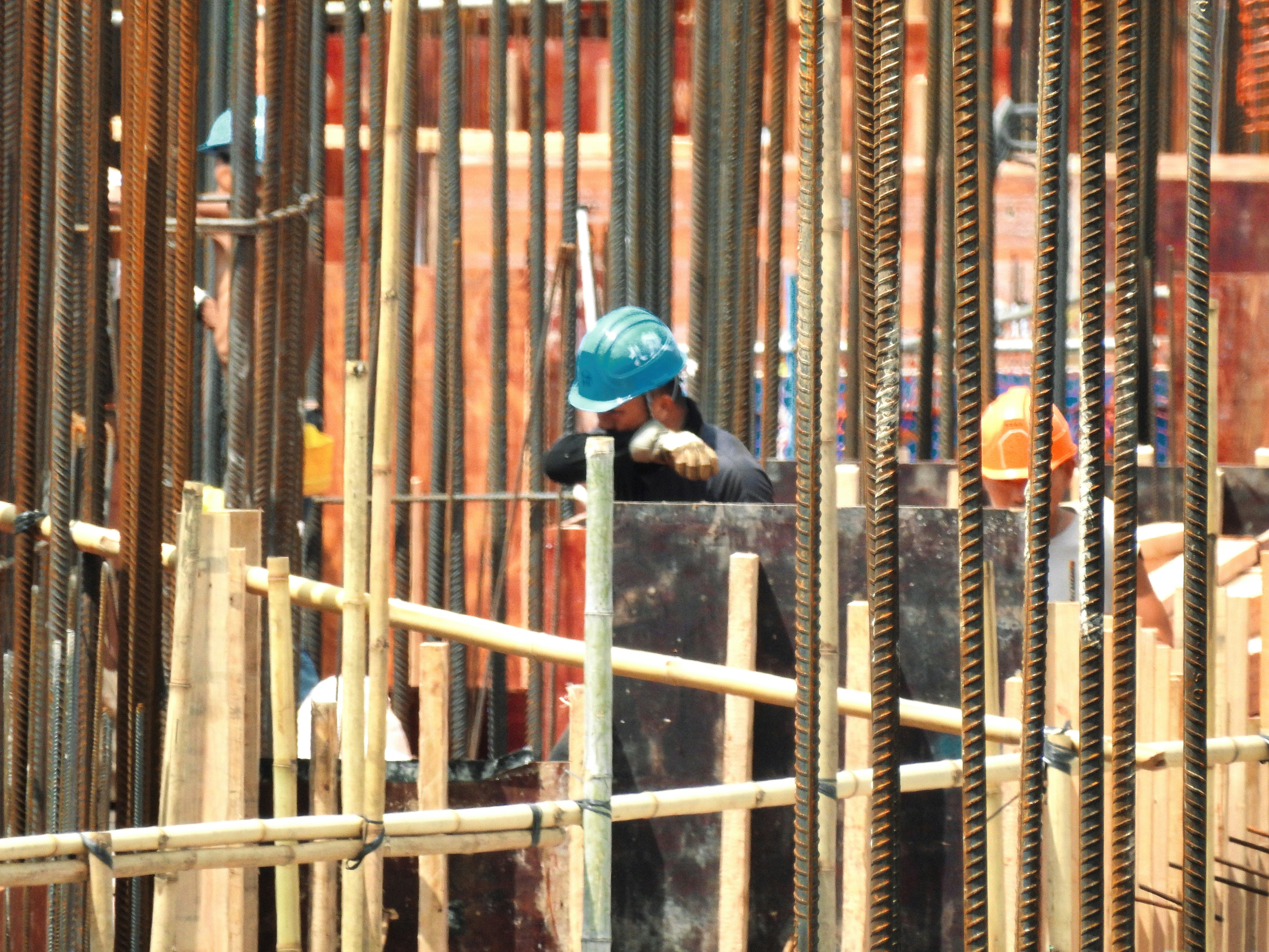 Construction workers in hard hats on an active building site with scaffolding and steel framing, dim industrial atmosphere, deep shadows, low-key site lighting