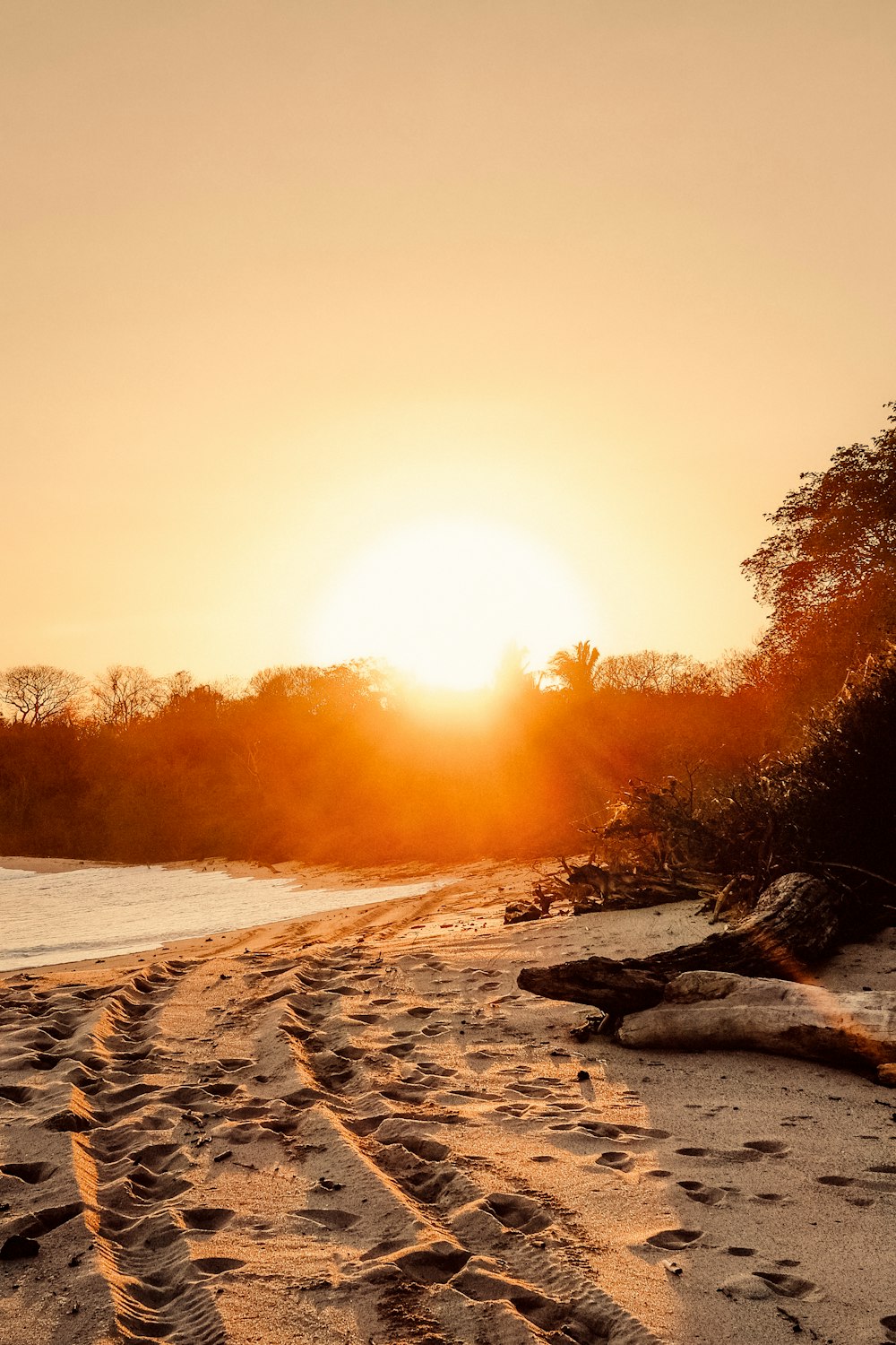 the sun is setting over a beach with tracks in the sand