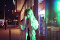 A dramatic night scene featuring a figure silhouetted by city lights, dressed in a long, dark trench coat.