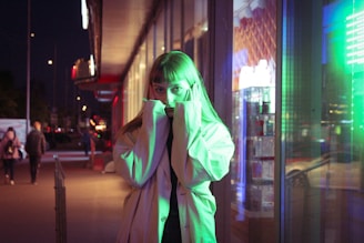 A dramatic night scene featuring a figure silhouetted by city lights, dressed in a long, dark trench coat.