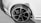 A close-up view of a car's front wheel, showcasing a sleek alloy rim and new tire on a clean, white vehicle. The image is in greyscale, emphasizing the shadows and highlights on the tire treads and rim spokes.