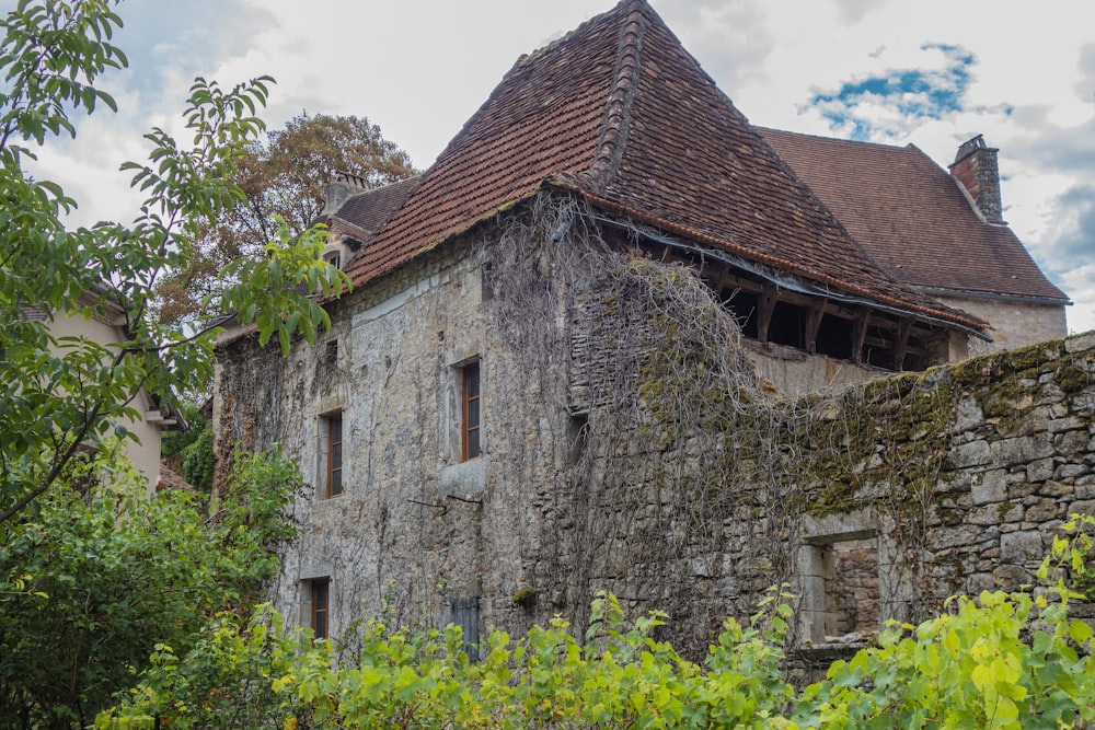 a stone building with a brown roof surrounded by greenery