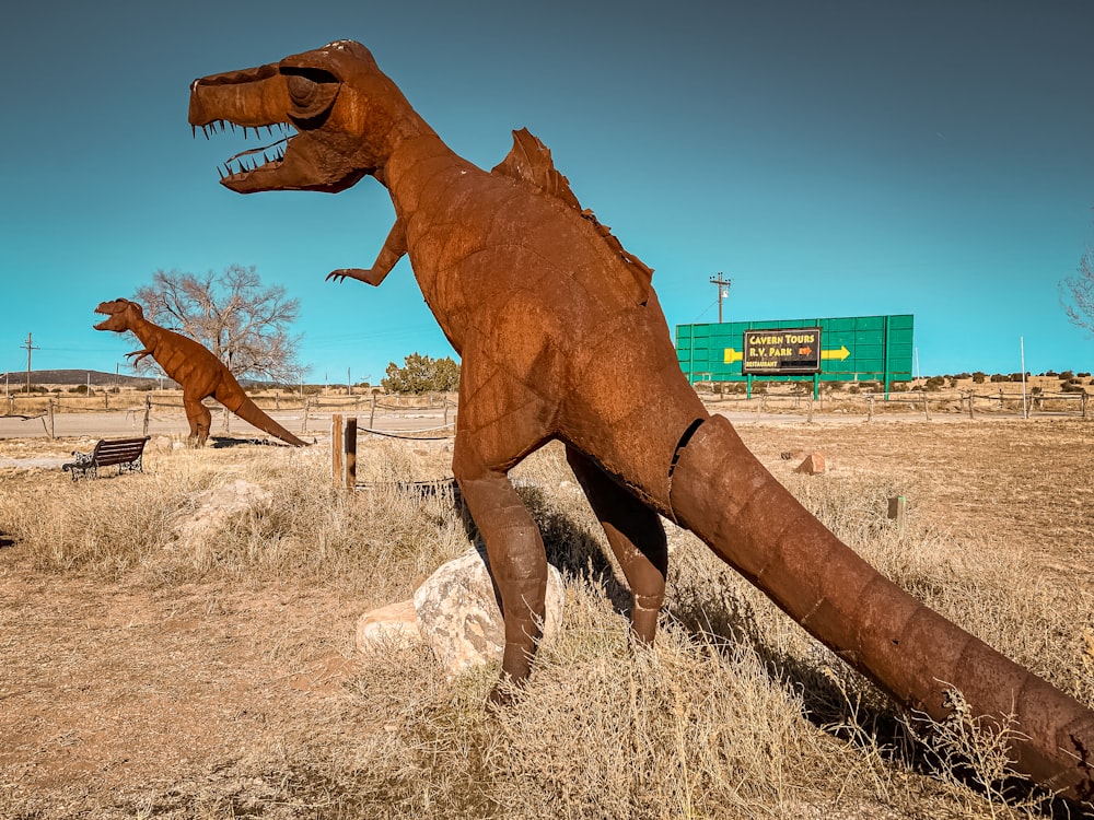 two fake dinosaurs in a field with a building in the background
