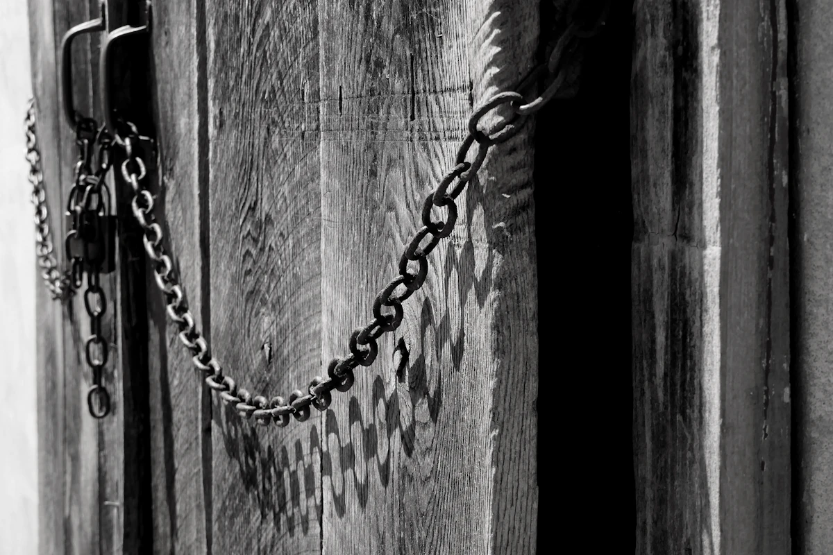 Foto hitam putih pintu kayu tua yang dirantai.
