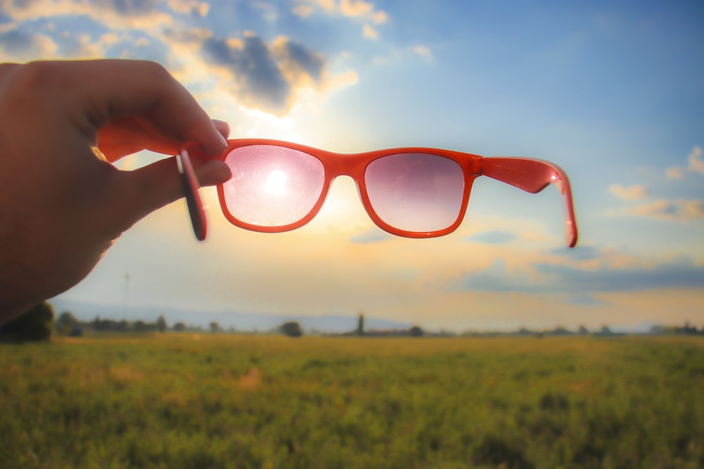 a person holding up a pair of red sunglasses