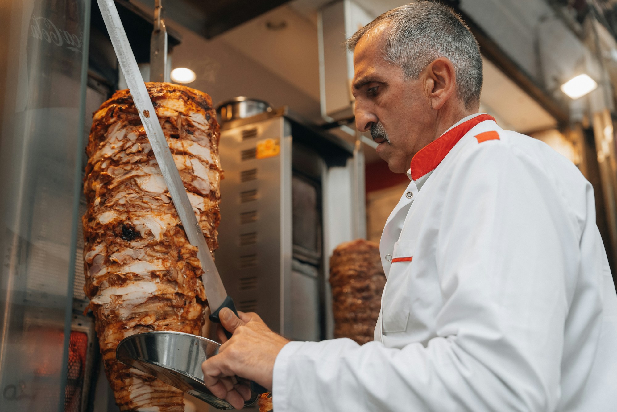 Beyaz önlüklü usta bir restoran mutfağında döner kesiyor