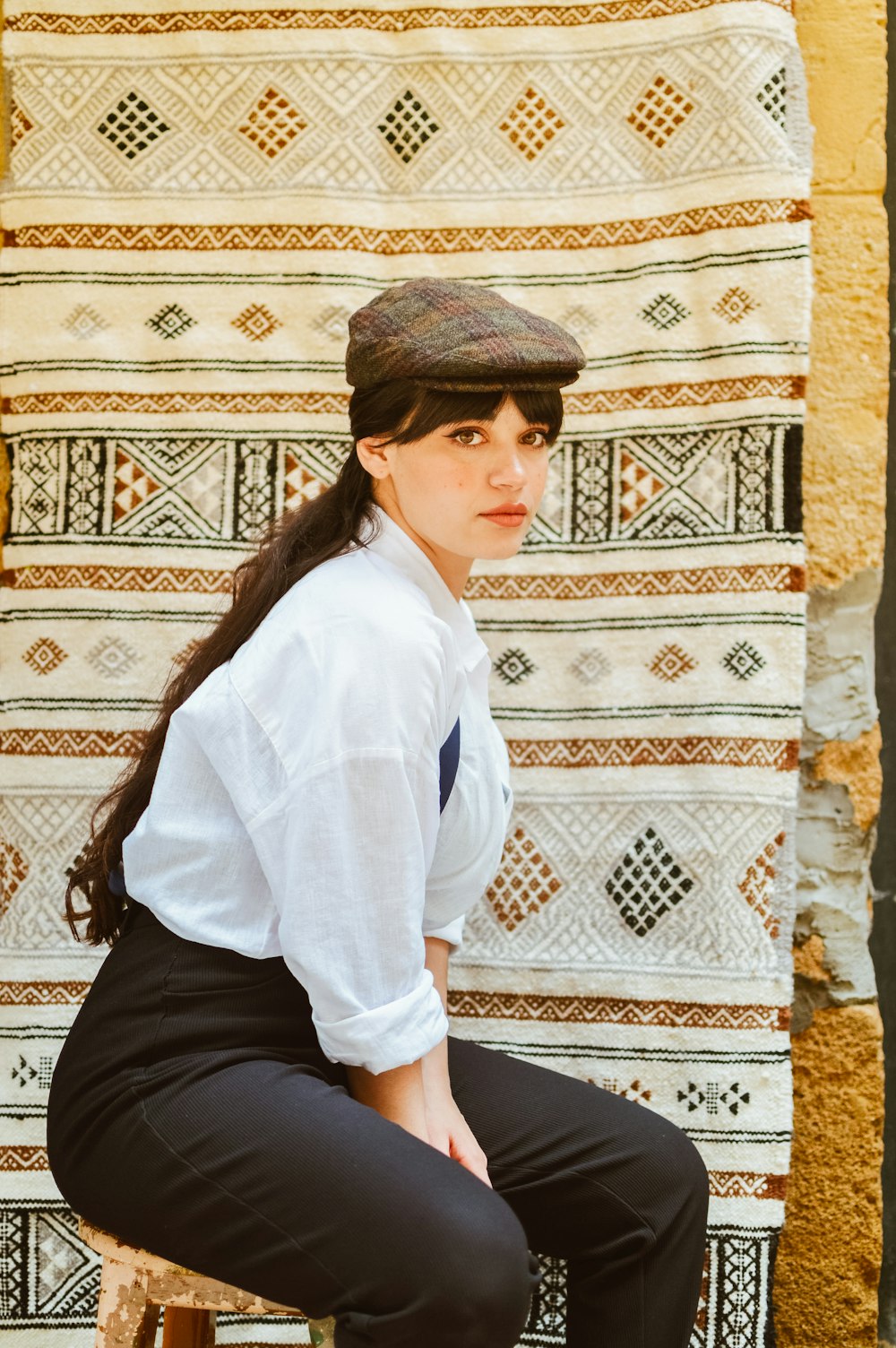 a woman sitting on a stool in front of a rug