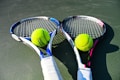 Two tennis rackets are lying on a court with tennis balls placed near the center of each racket. The rackets have blue and pink details with white grips, and the tennis balls are bright yellow.
