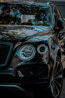 A luxury vehicle wrapped in a glossy black vinyl, reflecting ambient light against a dark backdrop.