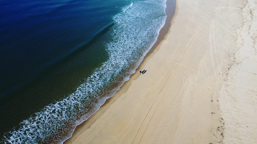 an aerial view of two people walking on a beach
