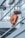 A close-up view of a metallic industrial hook system hanging from chains. The hook is painted orange and marked with '0.9t', indicating its load capacity. The background reveals the structure of a ship, with diagonal beams and a cloudy sky.