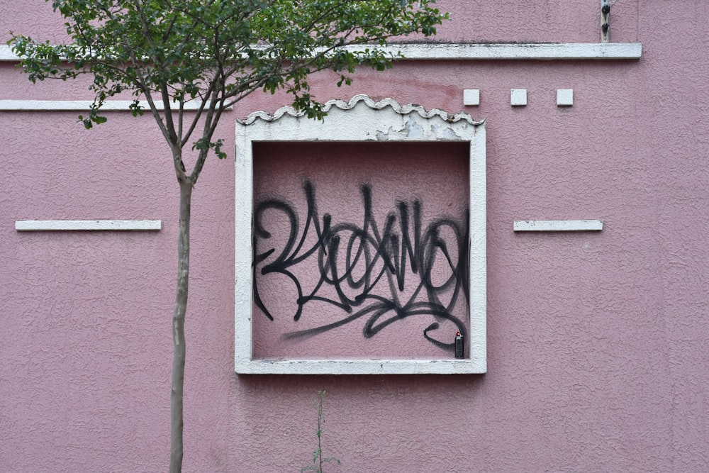 a pink building with graffiti on it and a tree in the window