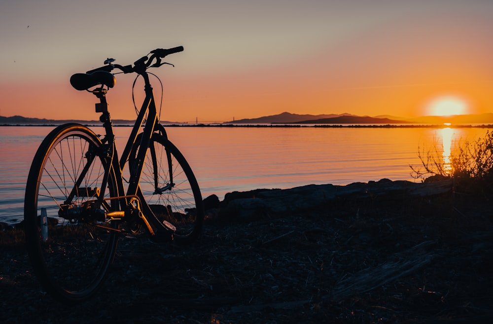 a bike parked next to a body of water at sunset