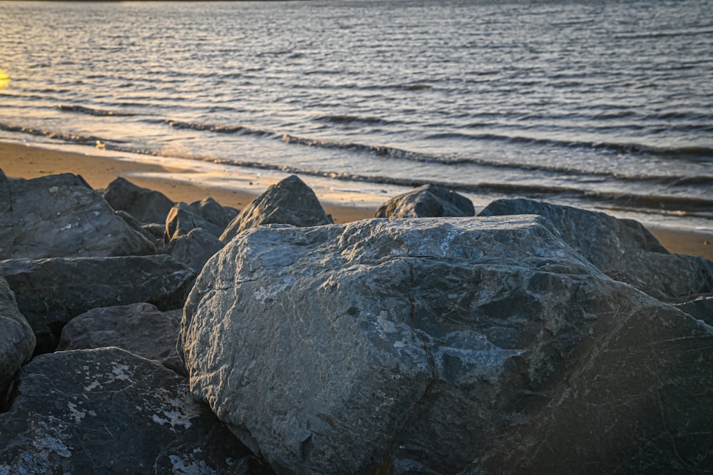 the sun is setting over the water and rocks on the beach