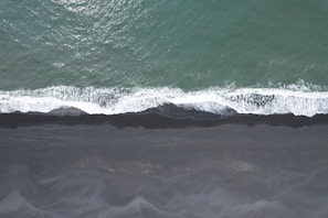 Deep ocean teal waves gently washing over smooth sand dotted with tiny seashells.