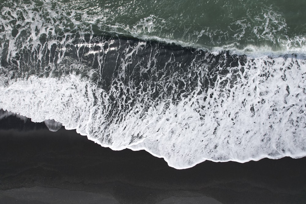 黒砂のビーチに打ち寄せる波の空撮